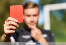 Referee holding up red sending off card. Image by Adobe.